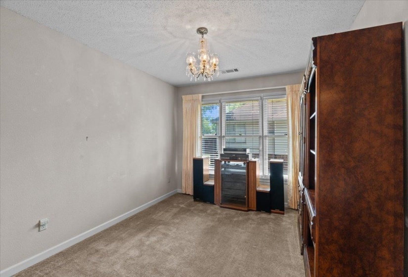 Carpeted interior space featuring a multi-pane window with blinds and drapes, a chandelier light fixture, and crown molding