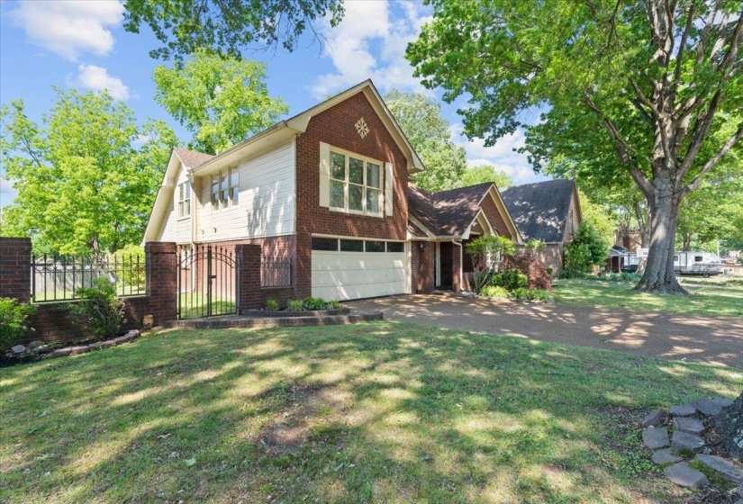 Traditional brick and siding exterior featuring a two-car garage, multiple windows, and mature trees