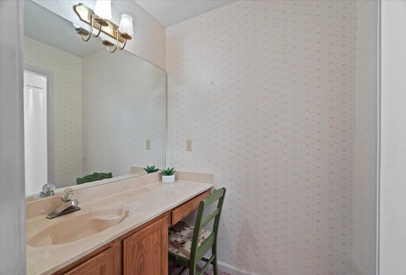 Bathroom vanity featuring an integrated sink, broad mirror, and brass-finish light fixture