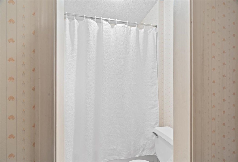 Compact bathroom featuring a white shower curtain and patterned wallpaper
