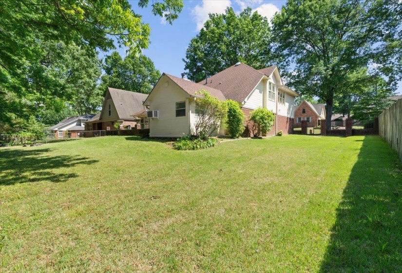 Spacious grassy lawn with mature perimeter trees, a wood privacy fence, and an established shrub border