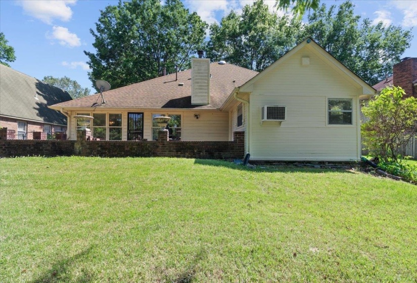 Expansive rear lawn featuring a brick patio, multiple windows, a light-colored siding exterior, and a gabled roofline