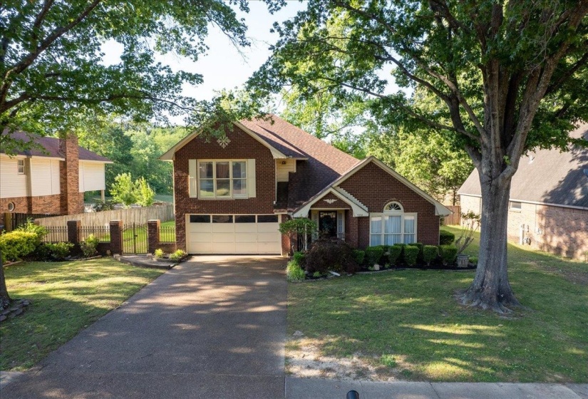 Brick exterior with a white garage door, featuring a paved driveway, manicured lawn, and mature trees