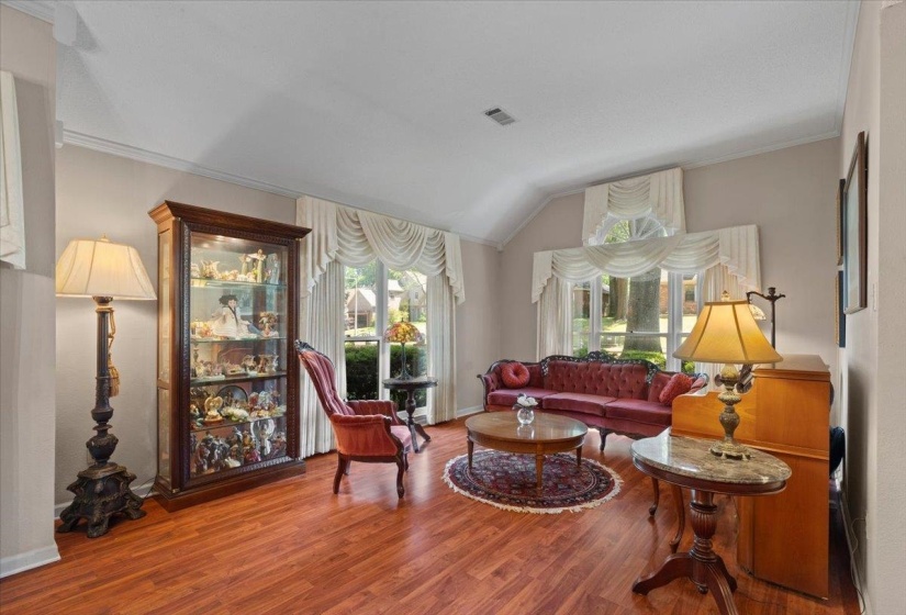 Spacious living area featuring wood-finish flooring, vaulted ceilings, and large windows with decorative valances