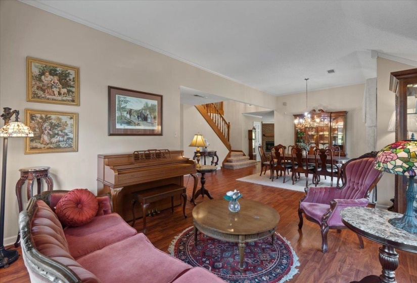 Open-concept living space featuring wood-finish flooring, a staircase with wood railings, a formal dining area with a chandelier, and light-toned walls