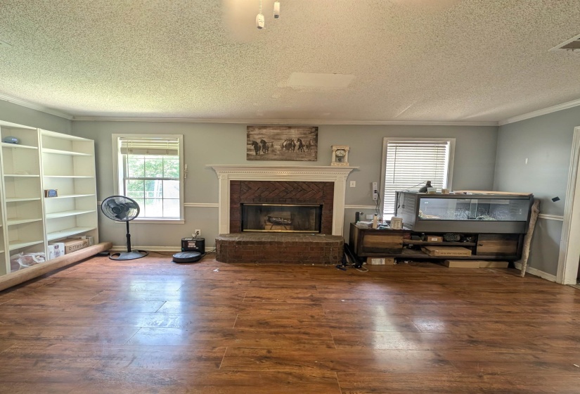 Spacious living area featuring wood-finish flooring, a brick fireplace with a white mantel, and built-in shelving