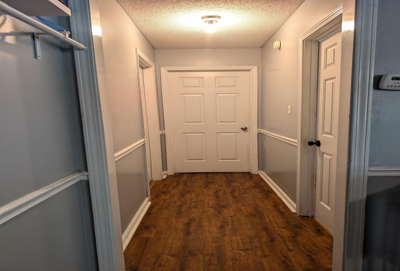 Hallway featuring wood-finish flooring, light gray walls with chair rail molding, white trim, and white panel doors with contrasting hardware
