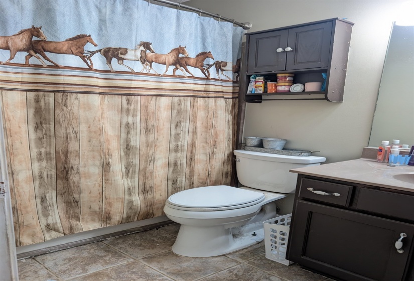 Bathroom featuring a built-in dark wood-finish vanity with a light countertop, a white toilet, and tile flooring