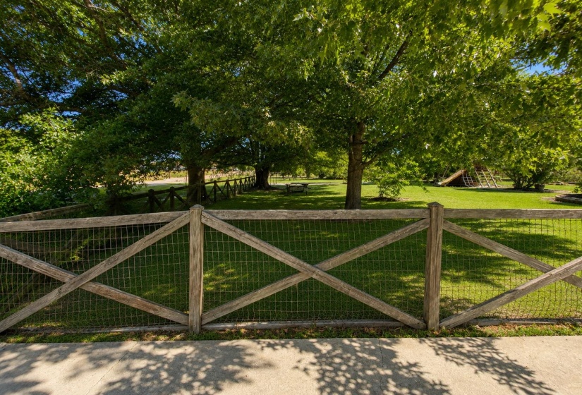 Expansive green space featuring a wooden fence with wire mesh, mature trees, and a concrete pathway