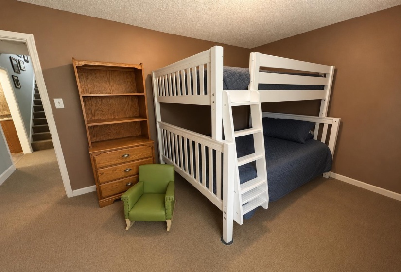 Carpeted room featuring a white bunk bed with integrated ladder, a wooden bookcase with drawer storage, and warm-toned wall paint