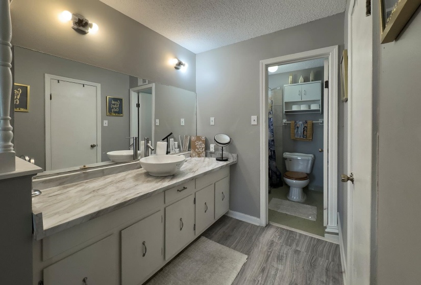 Bathroom vanity featuring dual vessel sinks, a spacious countertop with a marbled finish, and a large mirror with integrated lighting