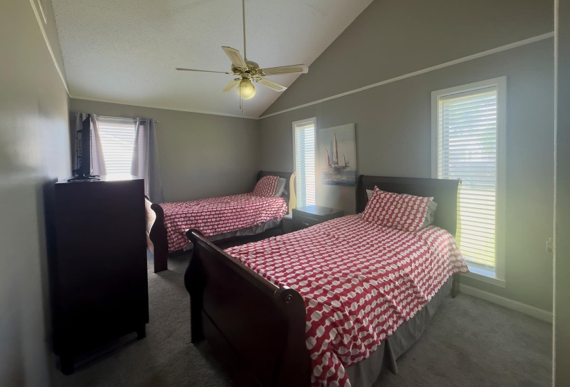Spacious room featuring a vaulted ceiling with a ceiling fan, two large windows with blinds, and neutral wall tones