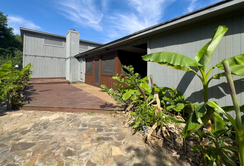 Exterior featuring a wooden deck, flagstone patio, screened-in porch, and lush tropical plantings