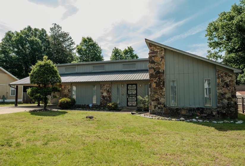 Mid-century modern residence featuring stone and vertical siding, a metal roof, and a prominent carport