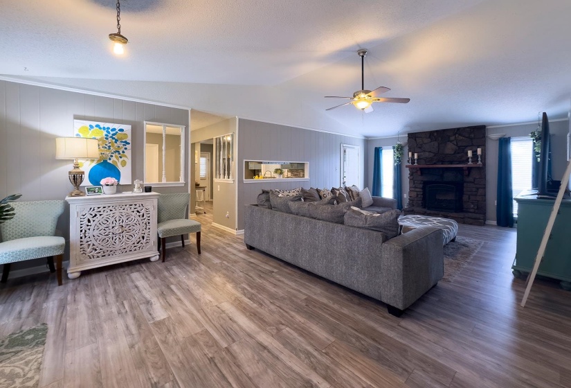 Spacious living area featuring wood-finish flooring, a stone-clad fireplace with a wood mantle, and a ceiling fan