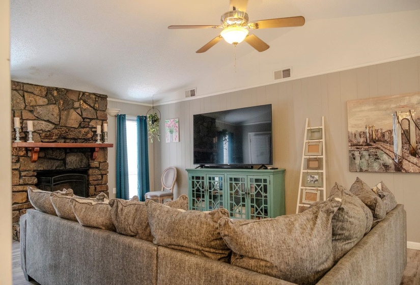 Living area featuring a stone-clad fireplace with a wood mantel, a ceiling fan with integrated lighting, and board and batten accent walls