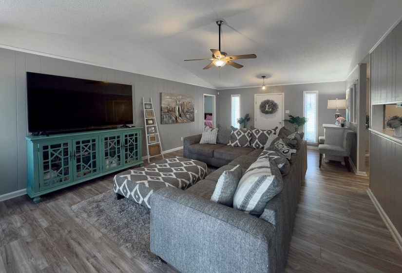 Spacious living area featuring wood-finish flooring, vaulted ceilings, and a ceiling fan with integrated lighting