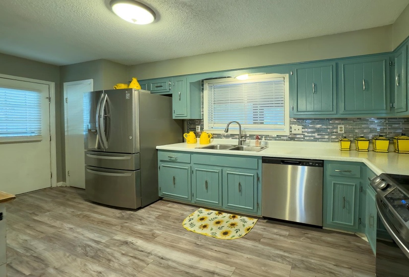 Kitchen with wood-finish flooring, custom teal cabinetry, light countertops, and a gray subway tile backsplash