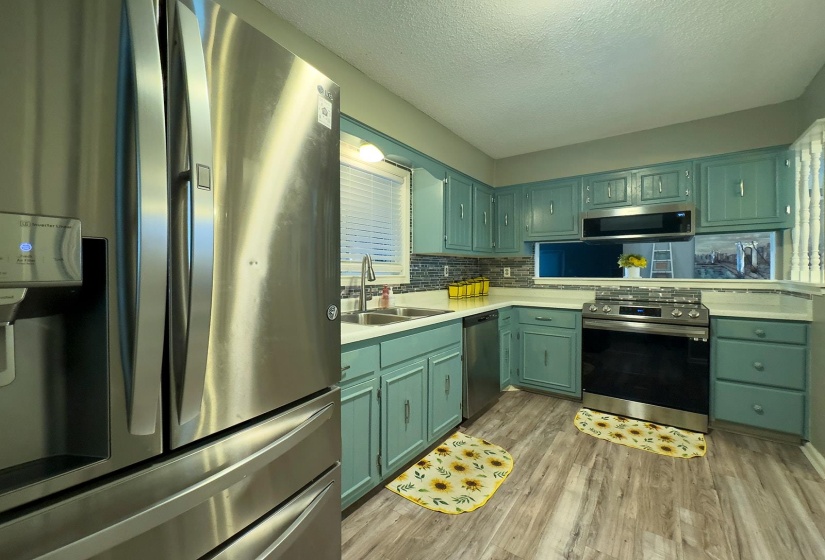 Kitchen featuring teal cabinetry, stainless steel appliances, wood-finish flooring, white countertops, and a mosaic tile backsplash