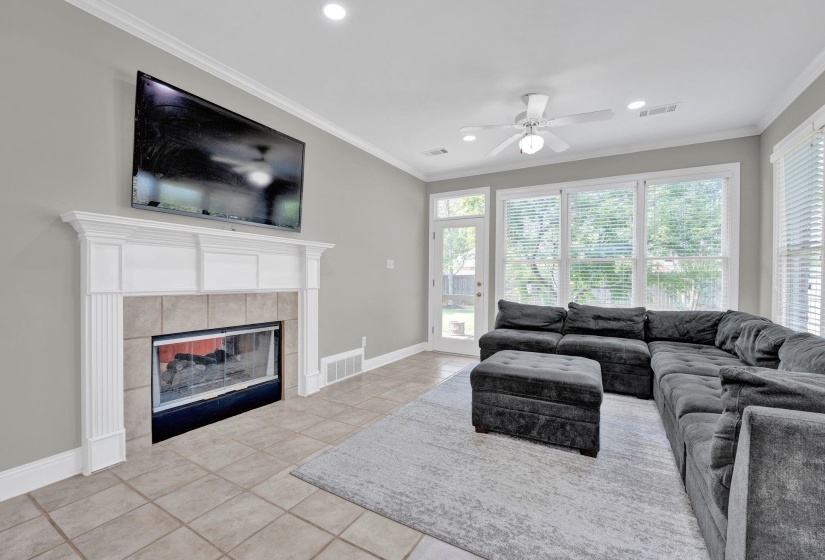 Living room featuring light tile patterned flooring, a fireplace, crown molding, and ceiling fan