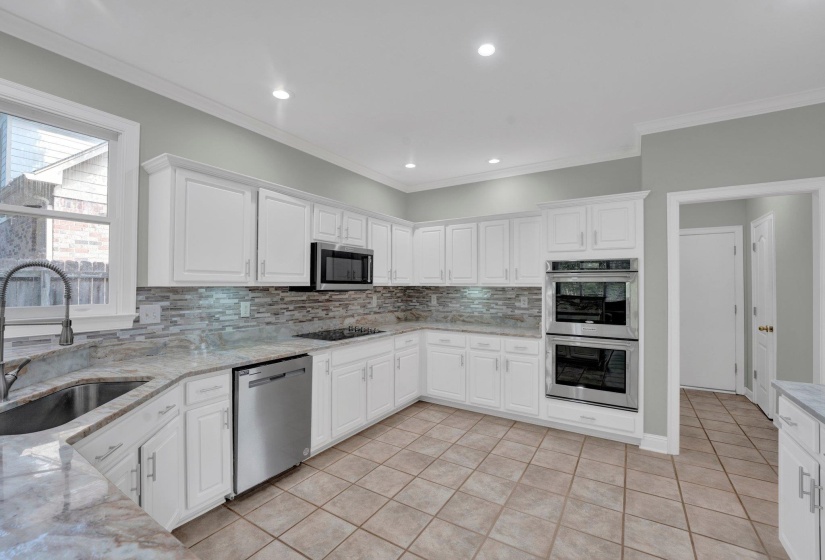 Kitchen with stainless steel appliances, white cabinets, sink, decorative backsplash, and light stone countertops