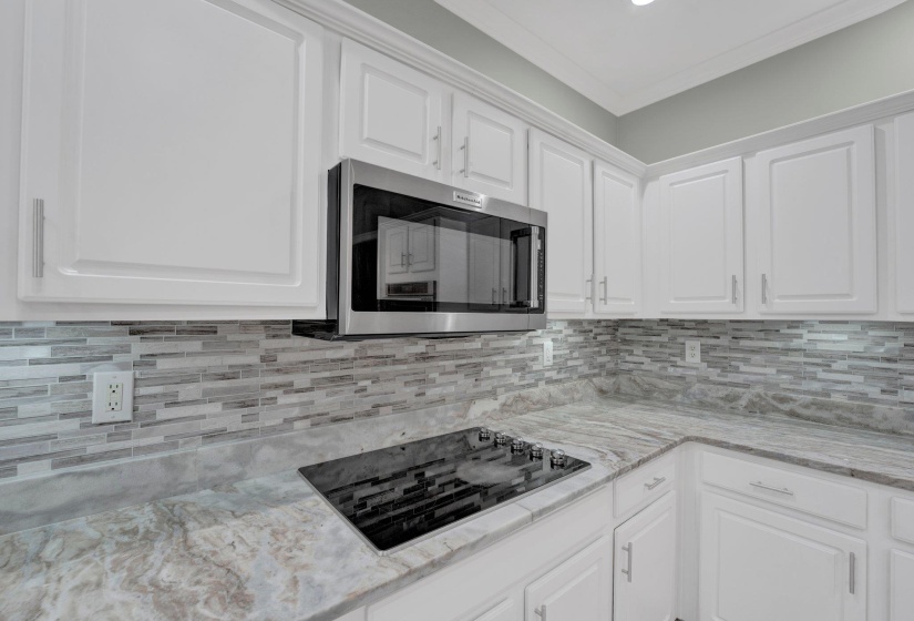 Kitchen featuring white cabinetry, backsplash, and black electric stovetop