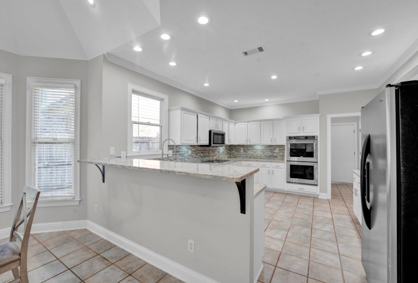 Kitchen featuring white cabinetry, stainless steel appliances, decorative backsplash, light stone counters, and light tile patterned floors