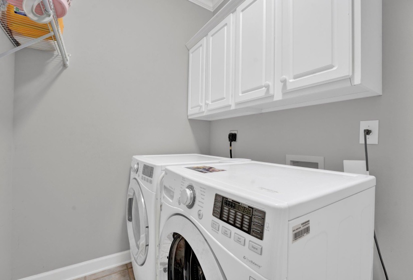 Clothes washing area featuring washing machine and dryer, cabinets, and light tile patterned floors