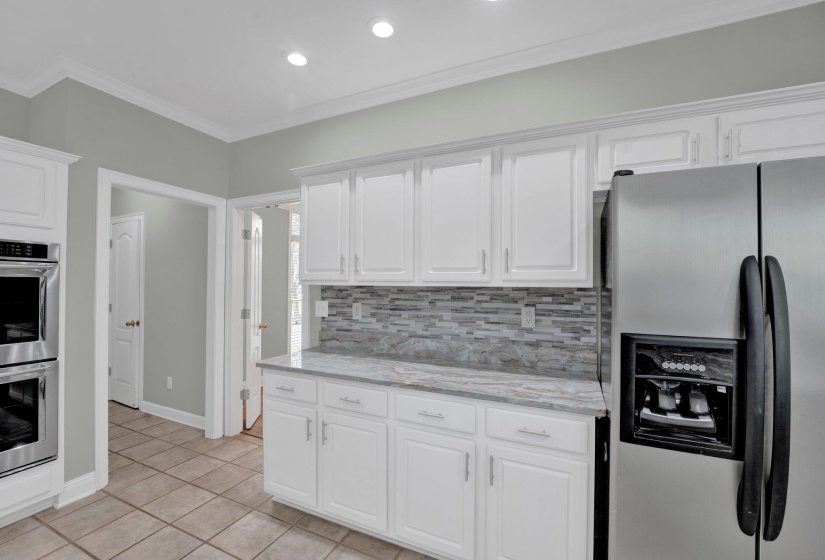 Kitchen with light tile patterned floors, white cabinets, appliances with stainless steel finishes, decorative backsplash, and ornamental molding