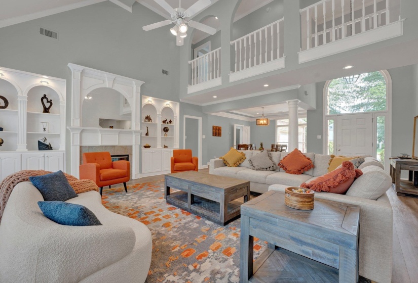 Living room featuring wood-type flooring, a tiled fireplace, ceiling fan, and a towering ceiling