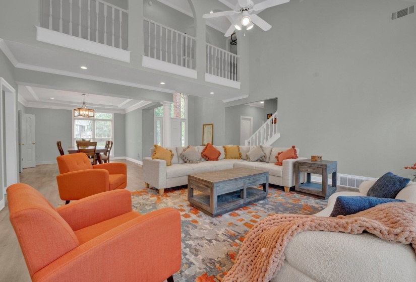 Living room featuring ornamental molding, ceiling fan with notable chandelier, and a high ceiling