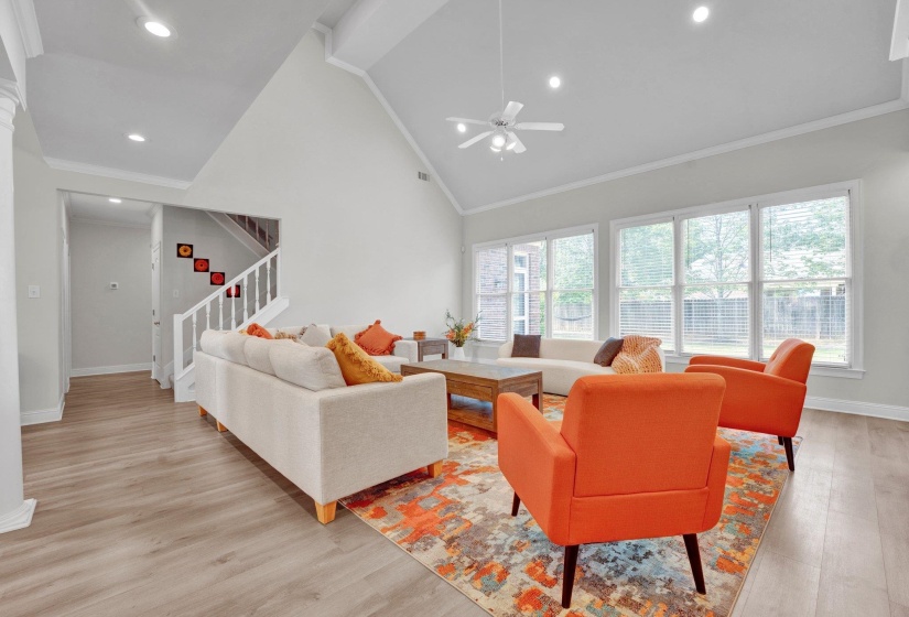 Living room with high vaulted ceiling, light wood-type flooring, ceiling fan, and ornamental molding