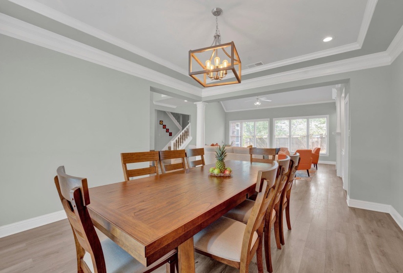 Dining room with ceiling fan with notable chandelier, ornamental molding, light wood-type flooring, and a tray ceiling