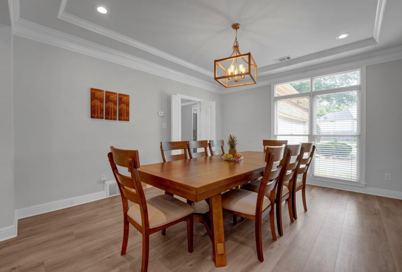 Dining area with a notable chandelier, light hardwood / wood-style flooring, crown molding, and a tray ceiling