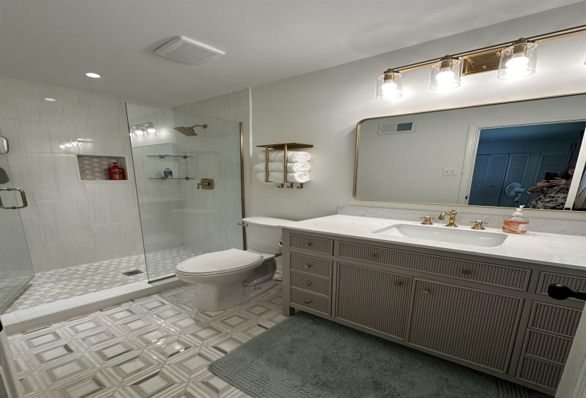 Contemporary bathroom featuring a glass-enclosed shower with tile surround and integrated niche, a single vanity with a white countertop, gold-finish fixtures, and geometric floor tiling