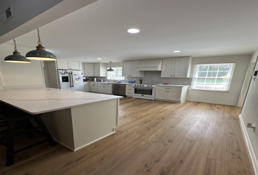 Kitchen featuring an island with a waterfall-edge countertop, wood-finish flooring, white cabinetry, a tile backsplash, and recessed lighting