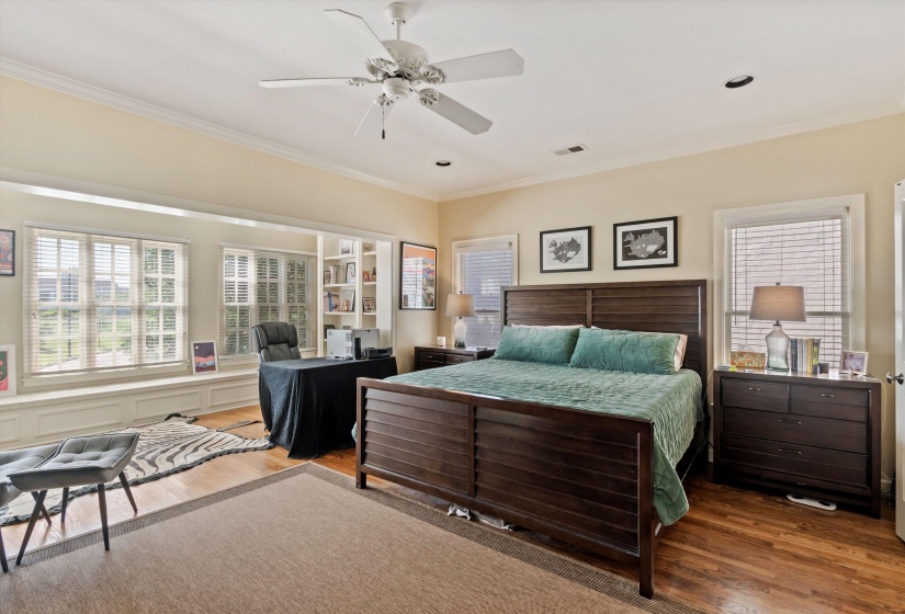 Spacious room featuring wood-finish flooring, multiple windows with blinds, built-in shelving, and crown molding