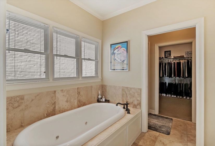 Built-in soaking tub with a tiled surround, three windows with blinds, and tile flooring