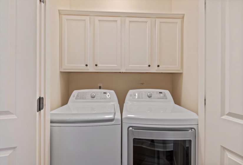Dedicated laundry area featuring custom cabinetry with dark hardware, a built-in shelf, and a light color palette