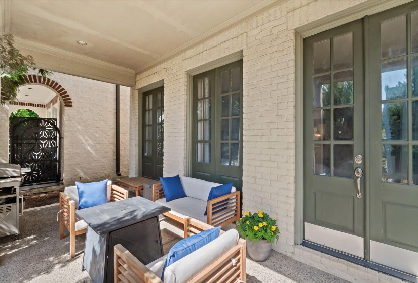 Covered patio featuring a painted brick exterior, dark green French doors, and an arched brick entryway with a decorative iron gate