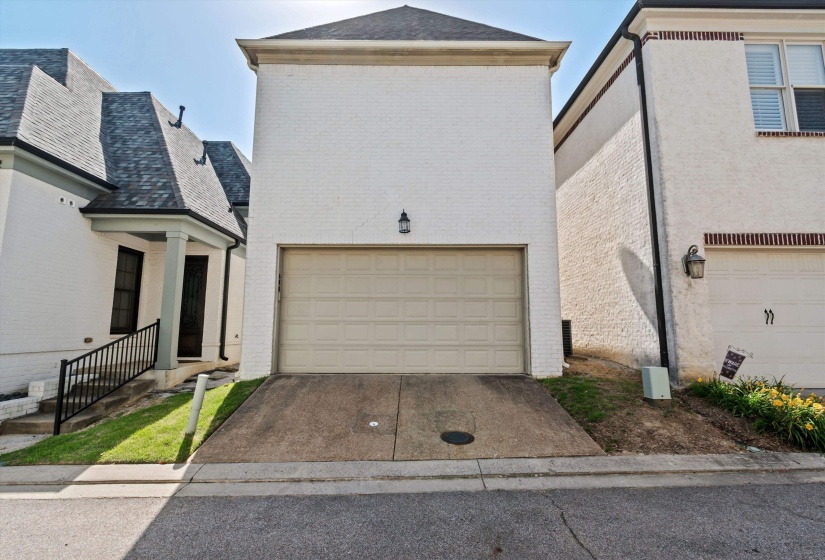 White brick exterior featuring a garage with a panel door, concrete driveway, and an exterior wall light fixture