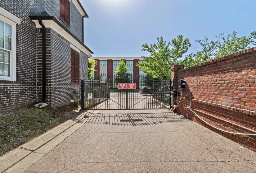 Gated driveway entrance featuring an automatic wrought iron gate and a full brick privacy wall