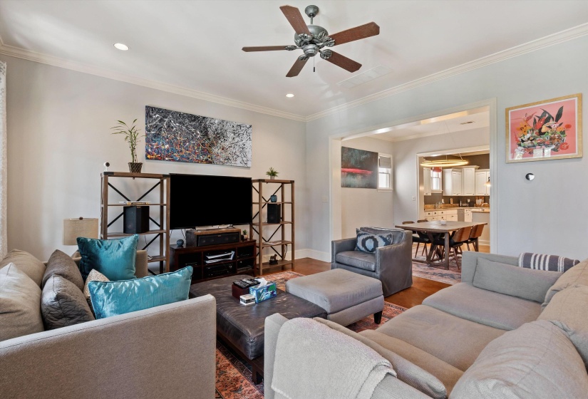 Recessed lighting illuminates this living area featuring wood-finish flooring and crown molding