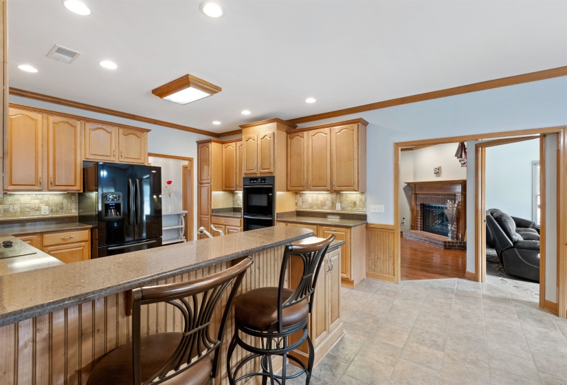 Kitchen featuring wood cabinetry, stone countertops, integrated black appliances, a breakfast bar, and tile flooring