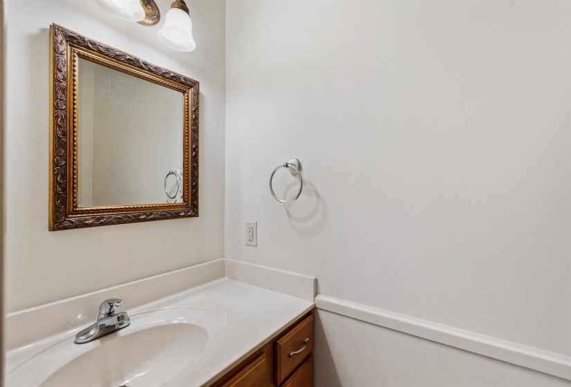 Vanity area featuring a framed mirror, a countertop with an integrated sink, a chrome faucet, wood-finish cabinetry, and overhead sconce lighting