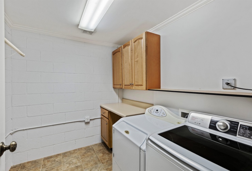 Laundry area featuring wood-finish cabinetry, a neutral countertop, tiled flooring, and crown molding