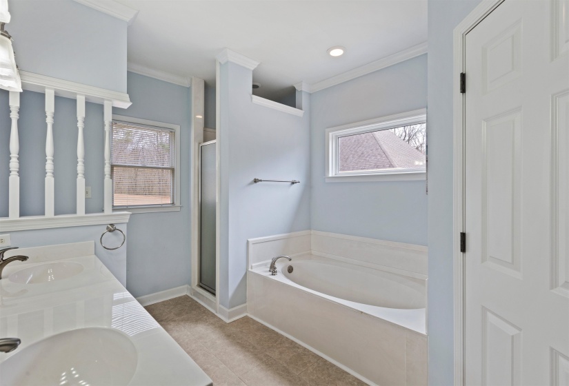 Bathroom featuring a dual vanity with integrated sinks, a built-in soaking tub, a glass-enclosed shower, and crown molding
