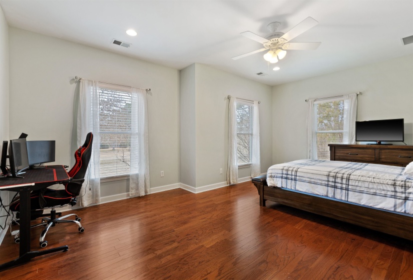 Spacious room featuring wood-finish flooring, two large windows with blinds, a ceiling fan with integrated lighting, and recessed lighting