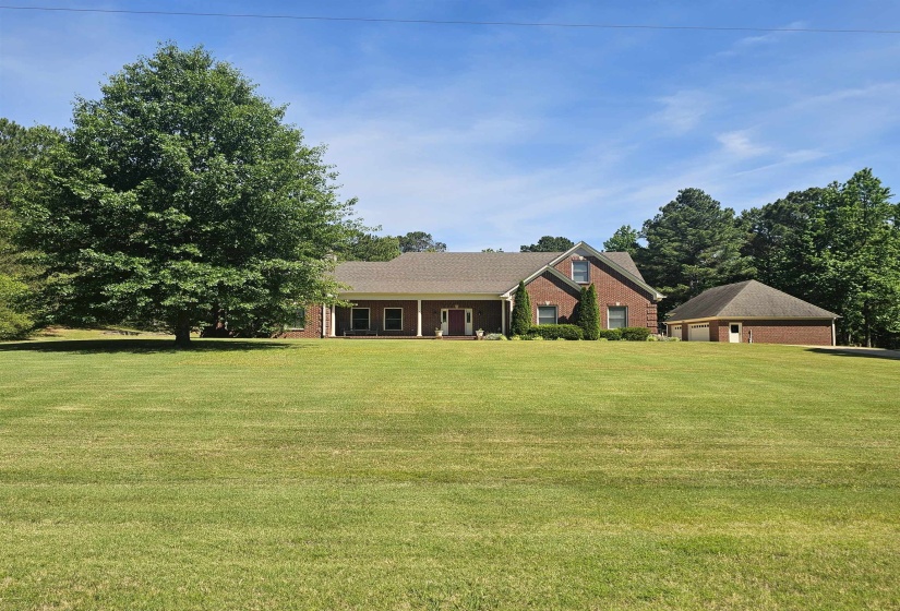 Expansive front lawn with a brick facade residence featuring a covered porch with white columns, a pitched roofline, and a detached two-car garage with a pyramid roof
