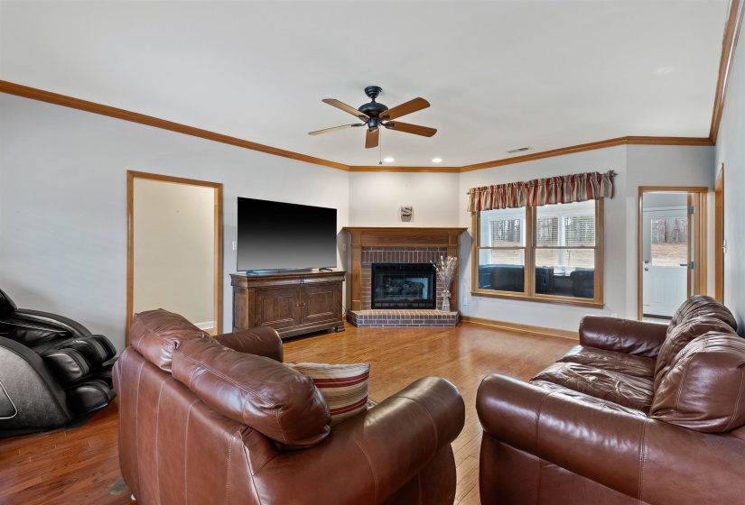 Living area featuring wood-finish flooring, a brick fireplace with a wood mantel, and multiple windows